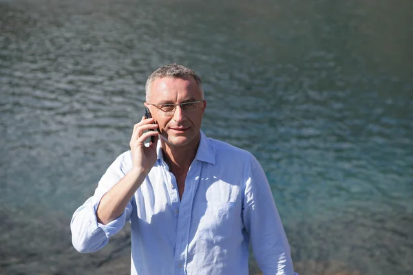 Empresário com um celular na frente da água — Fotografia de Stock