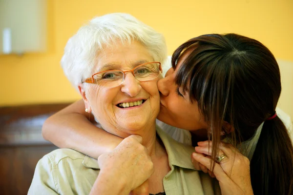 Porträt einer jungen Frau, die einer lächelnden Seniorin auf die Wange küsst — Stockfoto