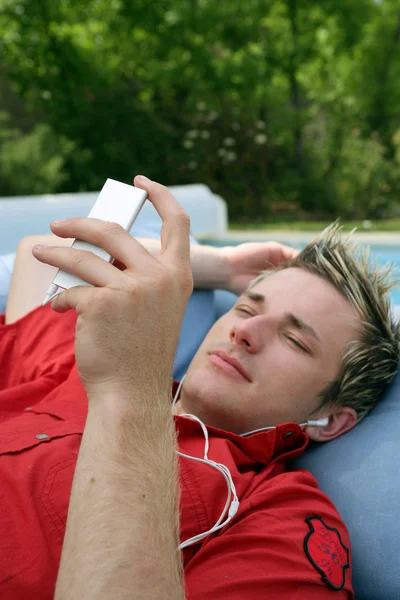 男子躺在花园听听音乐 免版税图库照片