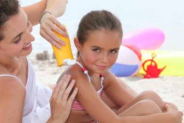 A mother putting sun cream on her daughter's shoulders clipart