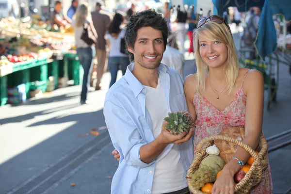 Pareja joven con una cesta de fruta en un mercado concurrido —  Fotos de Stock