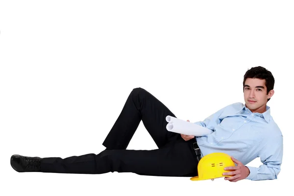 Mladý podnikatel leží na zemi a drží helmu a modrotisk — Stock fotografie