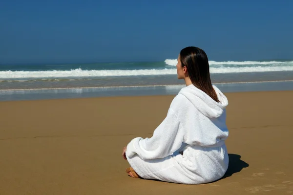 Mujer en un albornoz sentada en una playa — Foto de Stock
