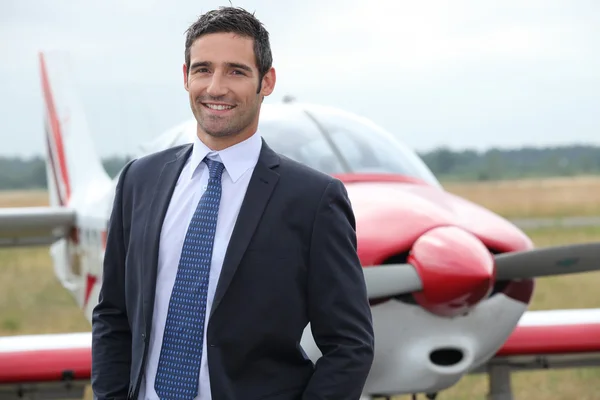 Χαμογελώντας επιχειρηματίας που στέκεται μπροστά από μια ελαφρά αεροσκάφη — Φωτογραφία Αρχείου