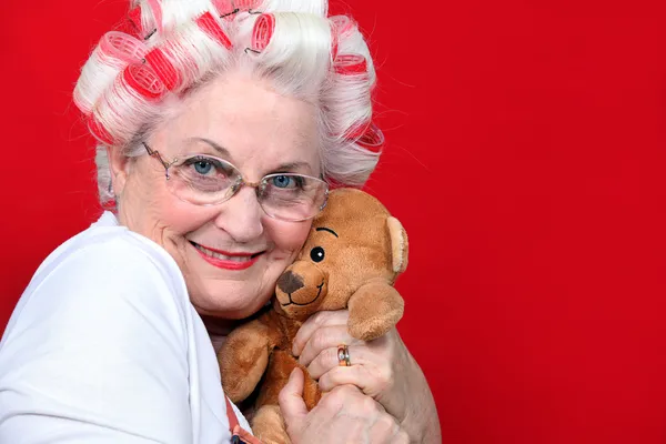 Eine alte Frau mit Haarrolle umarmt einen Teddybär. — Stockfoto
