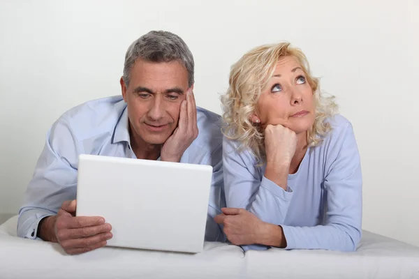 Couple d'âge moyen avec un ordinateur portable sur leur lit . — Photo