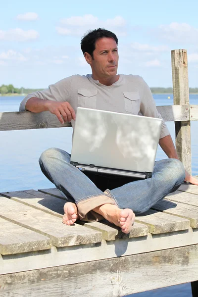 Homem no laptop perto de um lago — Fotografia de Stock