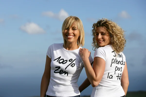 Women wearing slogan t-shirts against a blue sky — Stock Photo, Image