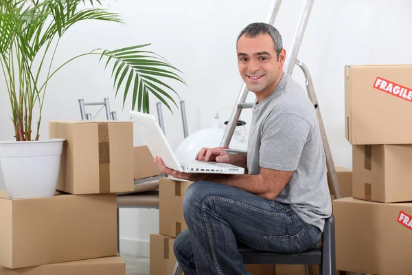 Homem usando um computador portátil sentado entre caixas de papelão — Fotografia de Stock