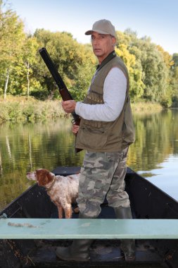 Hunter in a boat with a spaniel and a shotgun clipart