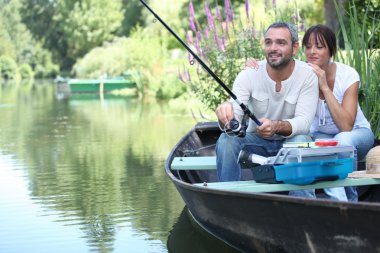 Couple fishing in a small boat on a river clipart