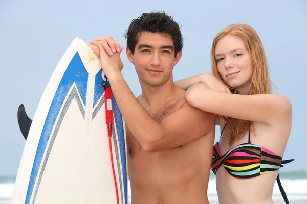 Pareja joven en la playa con tabla de surf — Foto de Stock
