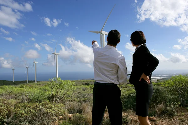 Casal de negócios em pé em um campo de turbinas eólicas — Fotografia de Stock