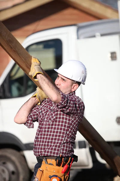 Trabalhador da construção civil carregando uma prancha pesada — Fotografia de Stock