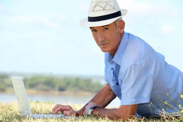 Старший мужчина лежит на траве перед ноутбуком — стоковое фото