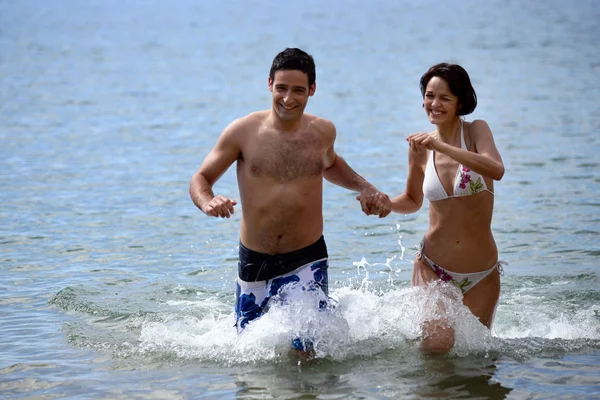 Casal correndo pela água de mãos dadas — Fotografia de Stock
