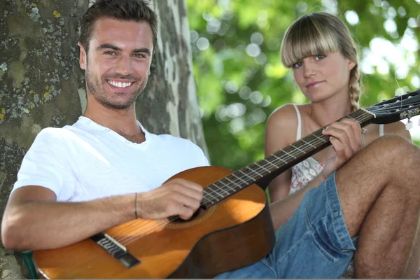 Чоловік з акустичною гітарою грає з дівчиною в парку — стокове фото