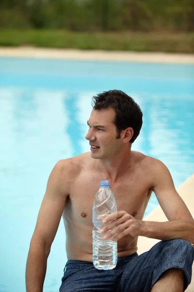 Homme à côté d'une piscine avec une bouteille d'eau — Photo