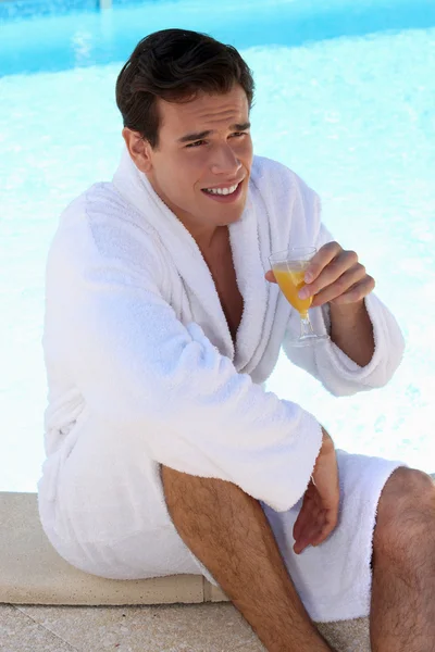 Muž pít pomerančový džus u bazénu — Stock fotografie