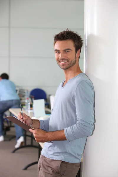 Чоловік в офісі, спираючись на стіну, тримає кишеню і ручку — стокове фото
