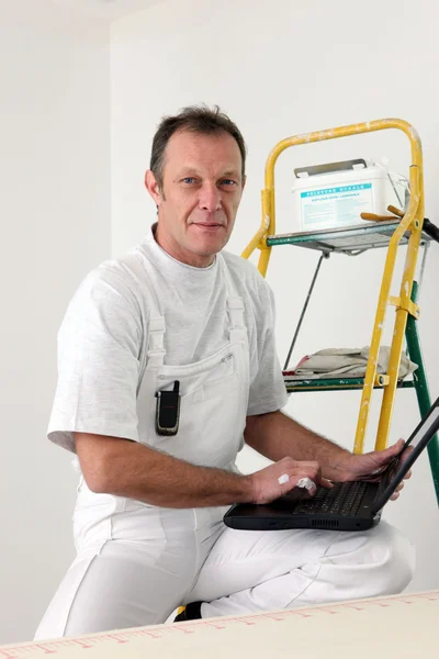 Pintor encaramado en la escalera mientras utiliza el ordenador portátil —  Fotos de Stock