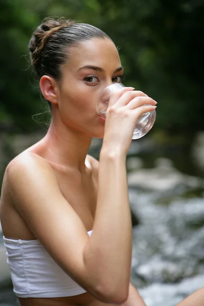 Mulher bebendo água por um riacho — Fotografia de Stock