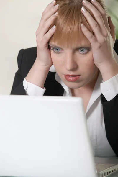 Mujer sosteniendo su cabeza en shock mientras mira una computadora portátil —  Fotos de Stock