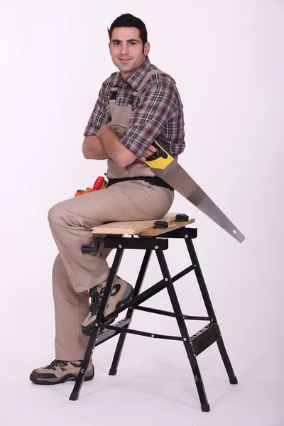 Trabalhador com serra sentado em uma bancada — Fotografia de Stock