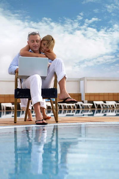 Casal olhando para um laptop por uma piscina — Fotografia de Stock