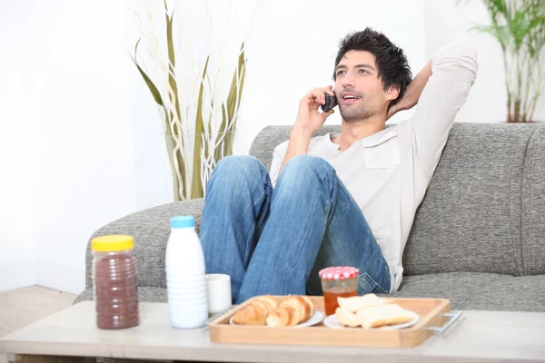 Молодой человек расслабляется на диване и разговаривает по телефону — стоковое фото