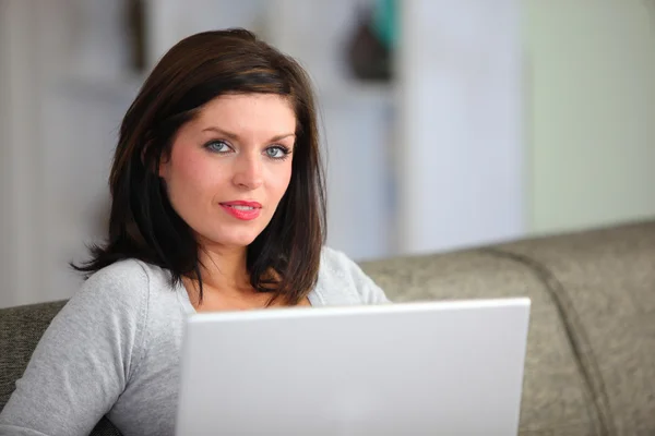 Женщина с компьютером сидит на диване — стоковое фото