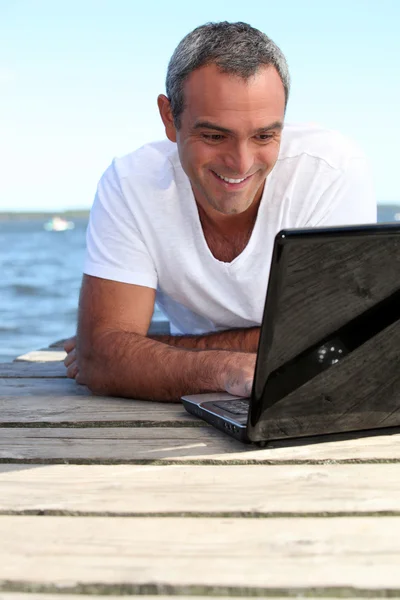Man using his laptop on jetty — Stock Photo, Image