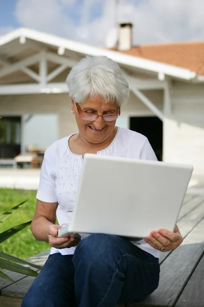 Starsza kobieta patrzy na laptopa na zewnątrz — Zdjęcie stockowe