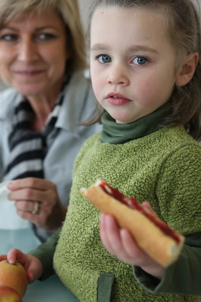 Little girl eating sandwich with mother — Stock Photo, Image