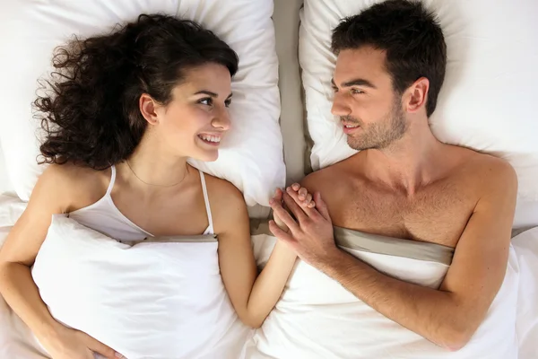 Jovem casal de mãos dadas na cama — Fotografia de Stock