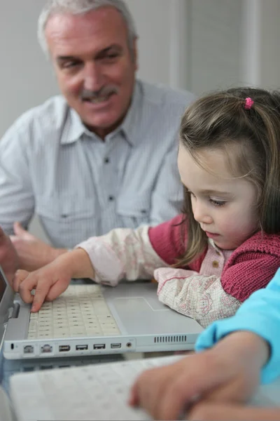 Kind op een laptop met haar grootvader — Stockfoto