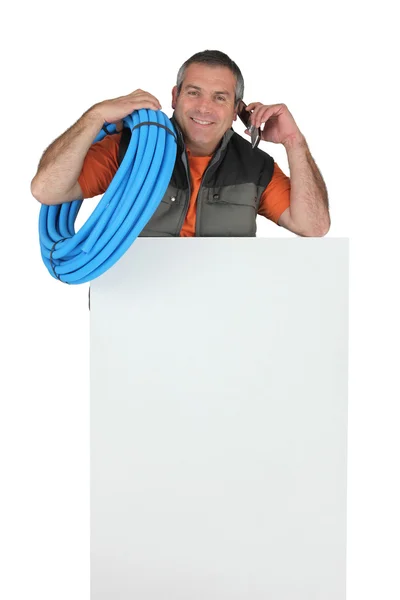 Electricista con rollo de tubo de plástico corrugado azul, un teléfono y una placa en blanco para su mensaje —  Fotos de Stock
