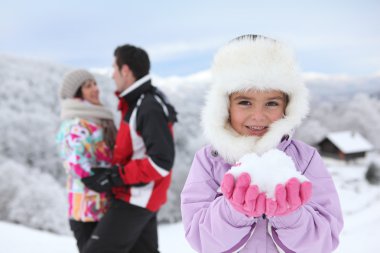 Little girl playing in the snow with her parents clipart