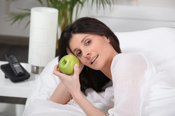 Mujer acostada en la cama con una manzana — Foto de Stock