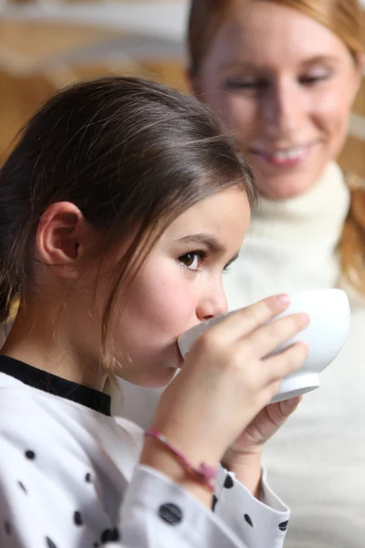 Mother watching daughter drink from bowl — Stock Photo, Image