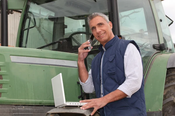 Agricultor perto de um trator com computador — Fotografia de Stock