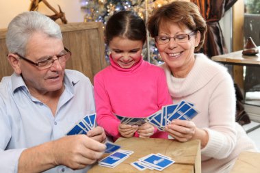 Little girl playing cards with her grandparents clipart