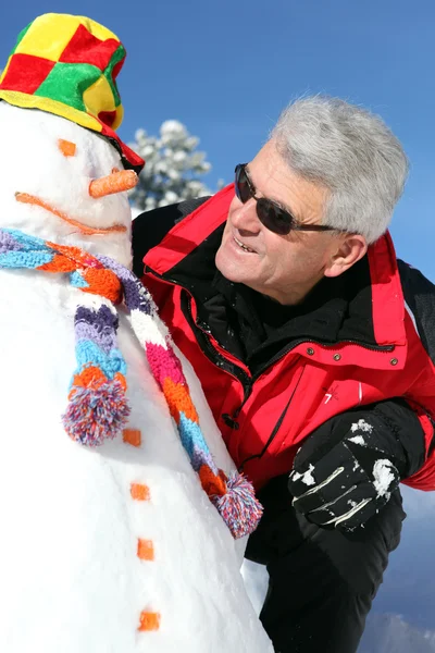 Senior man with a snowman — Stock Photo, Image