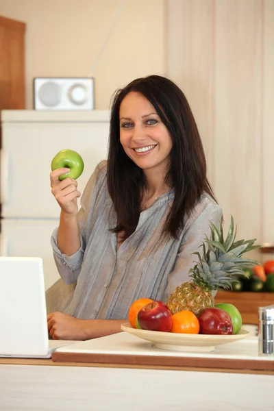 Žena s jablkem v kuchyni — Stock fotografie