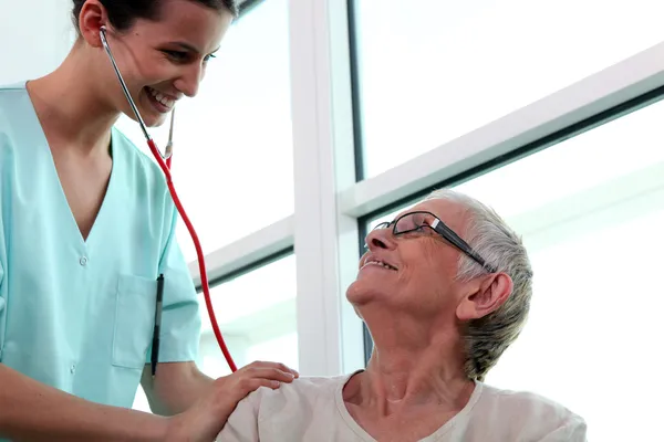 Enfermeira auscultando mulher idosa — Fotografia de Stock