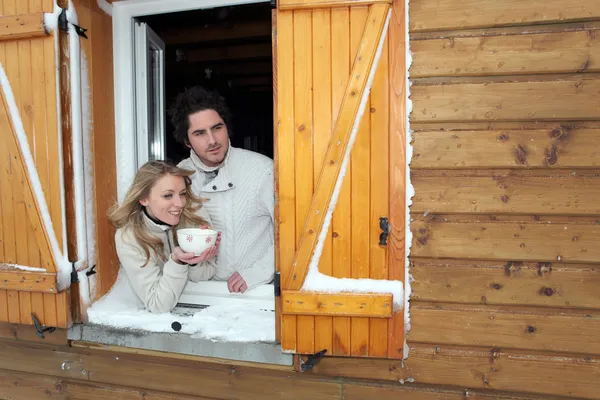 Couple looking out of their winter cabin — Stock Photo, Image