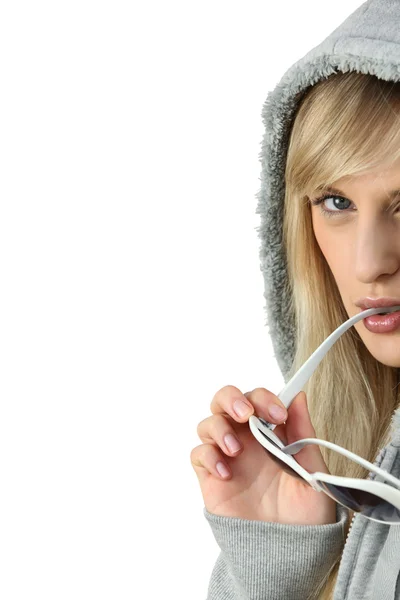 Woman in a sweatshirt with her sunglasses in her mouth — Stock Photo, Image