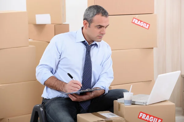Man omringd door kartonnen dozen met behulp van een laptop — Stockfoto