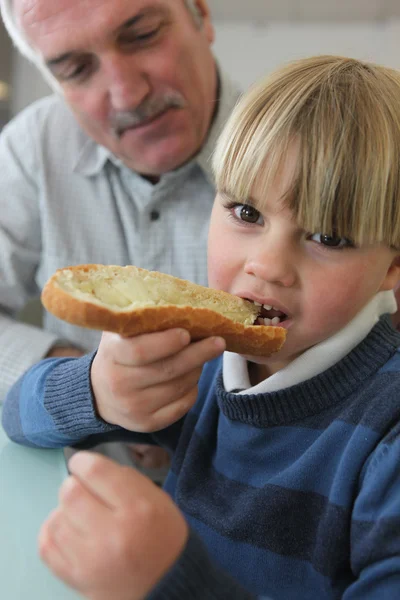 Boy eating bread with his grandfather — Stock Photo, Image