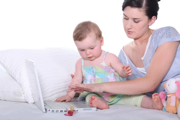 Мать держит ребенка и работает над ноутбуком — стоковое фото